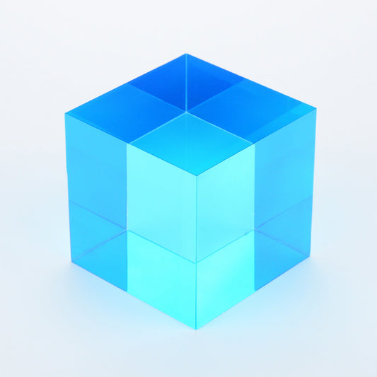A single cyan translucent cube on a white surface in direct sunlight